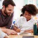 A teacher standing next to his student's desk and helping with schoolwork 