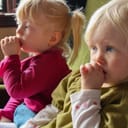 Two toddlers sucking their thumbs