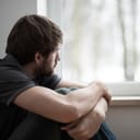 Sad young man sitting on the floor looking through the window