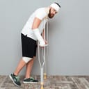 Badly hurt man with perplexed look on his face staring at the camera while leaning on crutches