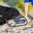 Close-up of a man using an air foot pump to inflate a mattress on a sandy beach.
