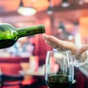 close-up of a woman's hand refusing more alcohol from a wine bottle in a bar