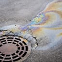 oil slick on asphalt road draining into a sewage system