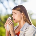 A woman holding a tissue in front of her mouth about to sneeze