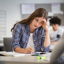 A worried student studying while holding her hand on the head