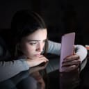 Sad female checking smart phone content in the dark night at home