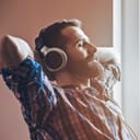 Man with calm expression on his face sitting on a chair wearing headphones with arms behind the head