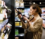 A woman in a supermarket reading a declaration on a wine bottle