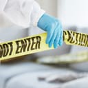 A close-up of a forensic investigator's hand at a crime scene in a house lounge, holding the evidence tape.