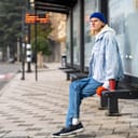 A young blond man waiting for transportation at a bus stop in the city.