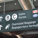 Signs at the airport display directing passengers to gates and the oversized baggage area.