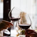 close-up of a young couple's hands toasting with glasses of red wine at a restaurant