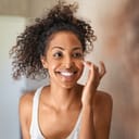 A smiling young African-American woman looking herself in the mirror putting on makeup