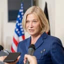 A middle aged woman holding a press conference in front of a US flag