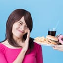 Woman refusing a plate of fast food offered to her containing fries, hamburger, sweets and glass of soda
