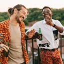 two male friends laughing and enjoying a rooftop party with beers
