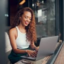 A smiling young woman typing on a laptop at a cafe