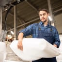 young male worker holding a heavy white sack in a warehouse