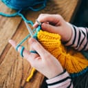 A woman knitting a yellow and blue sweater
