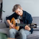 Middle-aged man sitting on couch playing acoustic guitar