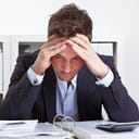 A stressed young man in a suit with his head buried in his hands