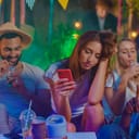 Disappointed girl looking at her smartphone as she sits among people at a party