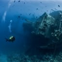 Shipwreck lying on the bottom of the seafloor with a scuba diver beside