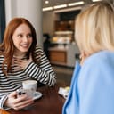 Two happy female friends engaged in conversation and in a café while drinking coffee