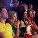 Young people sitting in multiplex movie theater, watching movie, eating popcorn.