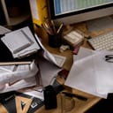 close-up of a messy office desk with disorganized piles of files and stationery