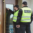 two male police officers knocking on a glass door of a suspect's home while on a duty