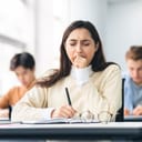Portrait of a tired female student yawning at her desk in a classroom, exhausted from studying for a test or writing coursework, and feeling sleepy during a high school lecture due to lack of sleep.