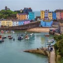 A small coastal town with different colored buildings, a beach and plenty of boats docked near the coast