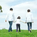 A little girl holding her parents' hands while walking in a park