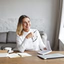 Happy middle-aged female editor reading a book at her desk and drinking coffee