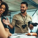 A male photographer holding a camera talking with his clients