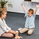 happy boy with raising hands and cute girl sitting on floor and playing blocks wood tower game in apartment