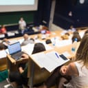 An audience attentively listening to the lecture in an amphitheater at a university.
