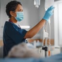Female nurse wearing a face mask is checking a patient's IV drip bag