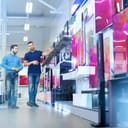 Consultant showing the latest 4K UHD TVs to a young man in a bright electronics store