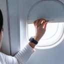 Close-up of a female passenger lifting the airplane window shade before landing.