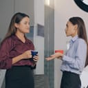Two businesswomen standing with coffee cups, enjoying casual conversation during a break.