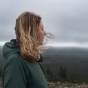 side-view portrait of a blonde woman looking at a forest with storm clouds