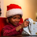 A young boy with a Santa Claus cap ripping open a present