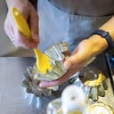 A closeup of a person greasing metal moulds using a brush