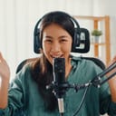 A smiling young woman with headphones on talking into a microphone