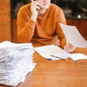 Person talking on the phone while going through a big pile of papers on a desk