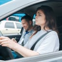 Worried young woman driving a car with the instructor by her side