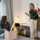 two female college students talking as one moves into a dorm room