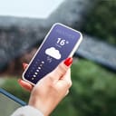 a female holding a mobile phone displaying the daily weather forecast